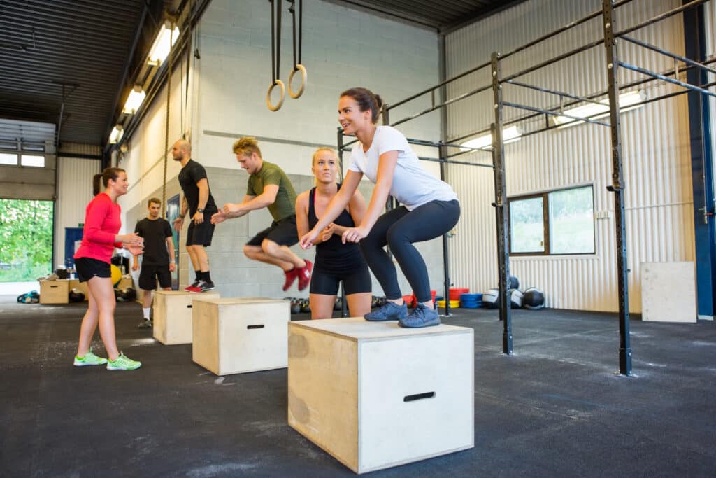Athlètes faisant des box jumps sur des boîtes en bois lors d'un entraînement de groupe dynamique en salle de sport.