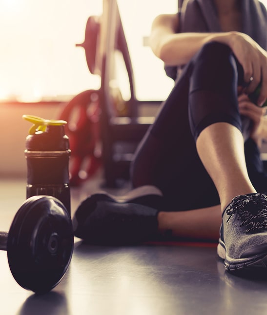 Femme assise au sol dans une salle de sport près d'un haltère et d'une bouteille, se reposant après l'entraînement fitness.