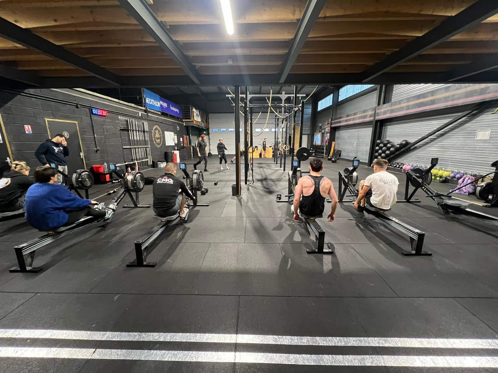 Des personnes s'entraînent sur des rameurs dans un gymnase. Équipements de fitness, textes DECATHLON et Foodspring.